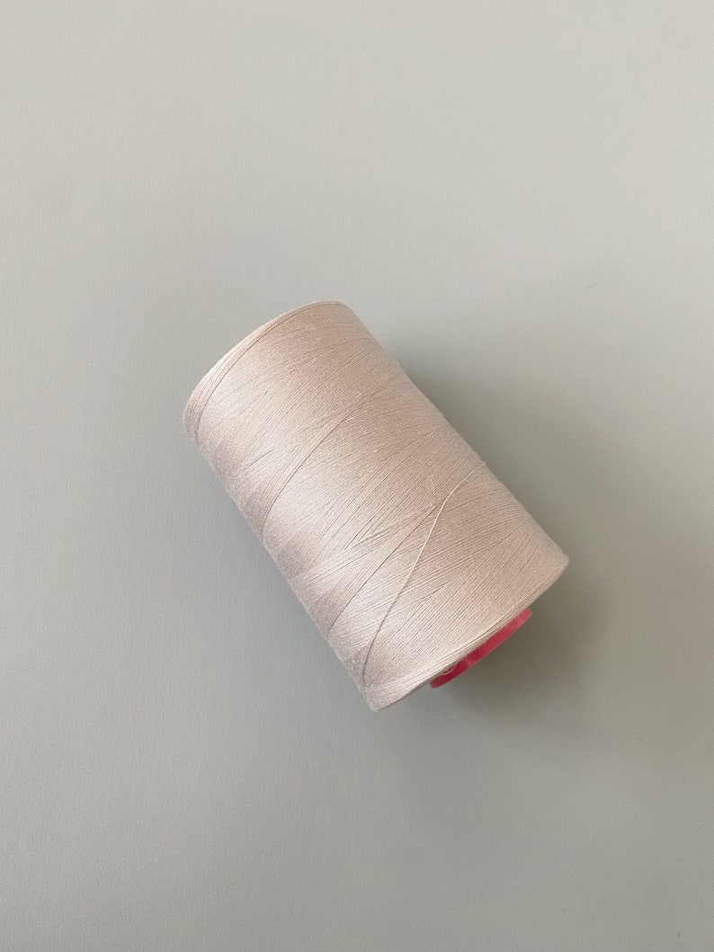 May include: A spool of white thread with a pink plastic bobbin.