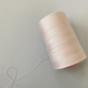 May include: A spool of off-white thread with a pink center, and a long strand of thread extending from the spool.