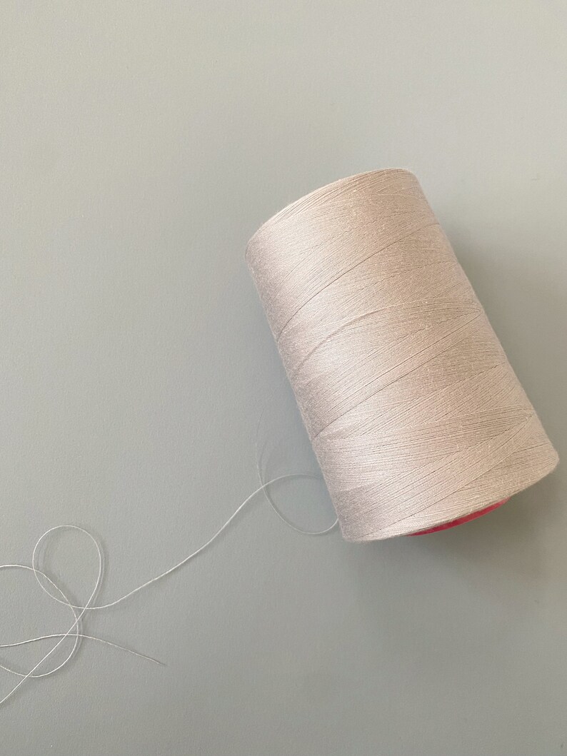 May include: A spool of off-white thread with a pink center, and a long strand of thread extending from the spool.