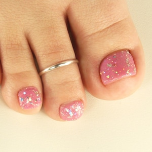 May include: A silver toe ring on a foot with pink glitter nail polish.