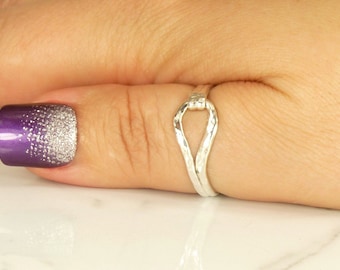 May include: A silver ring with a unique, twisted, open design. The ring is worn on a finger with purple and silver glitter nail polish.