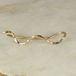 May include: A gold-toned, wavy, ear cuff earring. The ear cuff is made of a single piece of metal that is twisted and shaped into a wave-like design.