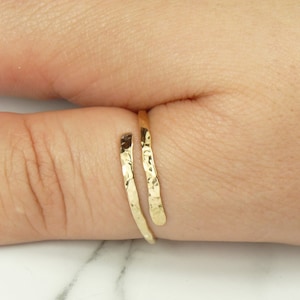 May include: A gold hammered thumb ring. The ring is made of a single piece of metal that is wrapped around the thumb.