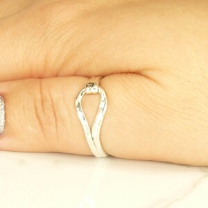 May include: A silver ring with a unique, twisted, open design. The ring is worn on a finger.