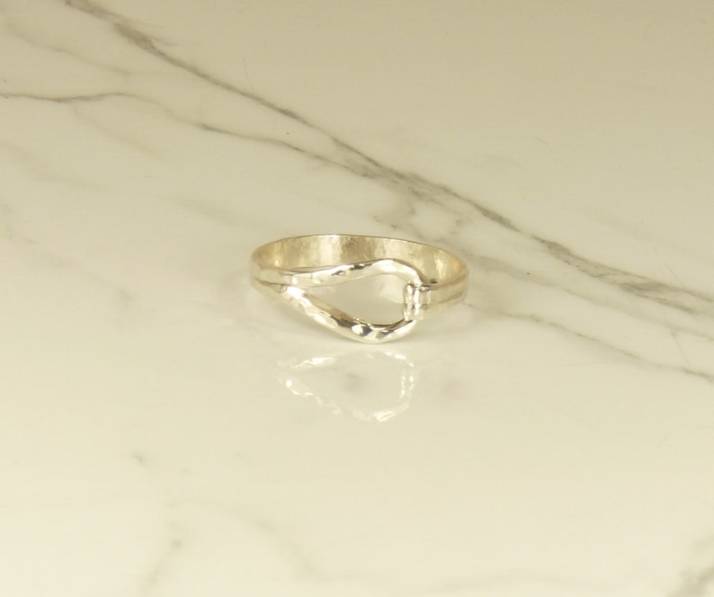 May include: A silver ring with a unique, hammered, open-loop design.