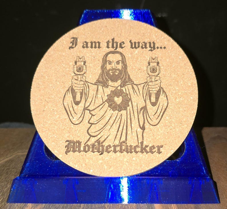 K&ouml;nnte beinhalten: Ein runder beigefarbener Korkuntersetzer mit einer dunkelbraunen Lasergravur einer b&auml;rtigen Figur in Roben, die zwei Handfeuerwaffen h&auml;lt. Der Text "I am the way..." steht &uuml;ber der Figur und "Motherfucker" ist darunter in Schwarz gedruckt.