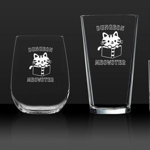 Könnte beinhalten: Vier klare Glas-Trinkgläser mit einem weißen Katzendesign und dem Text "Dungeon Meowster". Die Gläser sind in verschiedenen Größen und Formen.