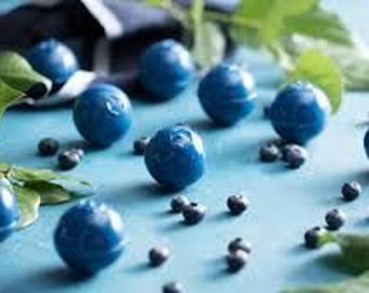 Könnte beinhalten: Nahaufnahme einer blauen Oberfläche mit mehreren blauen, blaubeerförmigen Süßigkeiten und grünen Blättern. Die Süßigkeiten sind auf der Oberfläche verstreut, und es gibt auch einige kleine, dunkelblaue Blaubeeren.