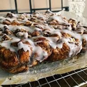 Könnte beinhalten: Eine große, rechteckige Form mit Zimtschnecken, die mit weißem Zuckerguss überzogen sind. Die Schnecken sind dicht aneinander gereiht und mit einer dicken Schicht Zuckerguss bedeckt.