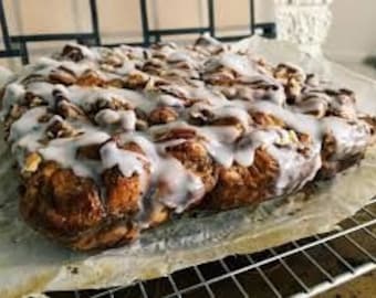 Puede incluir: Una bandeja rectangular grande de rollos de canela con un glaseado blanco. Los rollos están dispuestos en un patrón apretado y están cubiertos con una gruesa capa de glaseado.