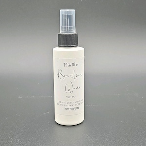 May include: A white spray bottle with a black cap and clear top. The label reads "R&W Brazilian Waves Toilet Spray." The bottle is on a grey surface. The product is designed to eliminate bathroom odours.