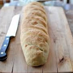 Puede incluir: Una hogaza de pan larga y dorada sobre una tabla de cortar de madera con un cuchillo plateado a su lado.