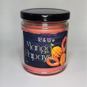 Puede incluir: Una vela de mango y papaya de color rosa en un frasco de vidrio con tapa negra. La etiqueta presenta un fondo negro con textura de madera y el texto "R&W co. Mango Papaya". La etiqueta también presenta una rodaja de mango y papaya.