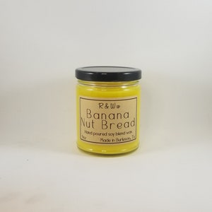 May include: A yellow candle in a glass jar with a black lid. The label is brown with white text that reads "R&Ww Banana Nut Bread Hand poured soy blend wax 9oz Made in Burleson, Tx."