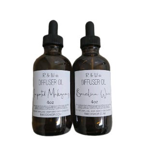May include: Two 4 ounce amber glass bottles of diffuser oil with black dropper tops. The bottles are labelled "R & W co. DIFFUSER OIL" with the scents "Imported Mahogany" and "Brazilian Woods".