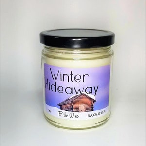 May include: A 9 oz candle in a glass jar with a black lid. The label is purple and blue with a white cabin and the text "Winter Hideaway". The text "R & W co." and "RWCOSHOP.COM" are also on the label.