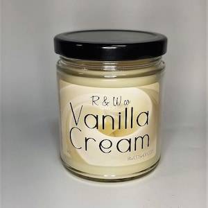 Puede incluir: Una vela de vidrio en un frasco con tapa negra y una etiqueta blanca que dice "R & W co Vanilla Cream" y "RWCOSHOP.COM".