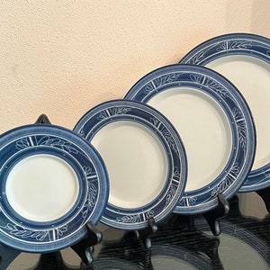 May include: Set of four blue and white ceramic plates with a decorative leaf pattern. The plates are arranged in size order, with the smallest plate in the front and the largest plate in the back.