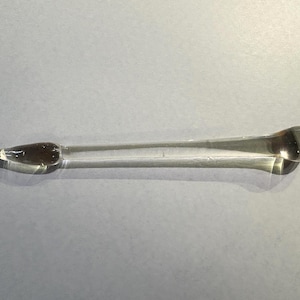 May include: A clear glass pipette with a bulb at one end and a pointed tip at the other. The pipette is filled with a dark brown liquid. The pipette is used for transferring small amounts of liquid.