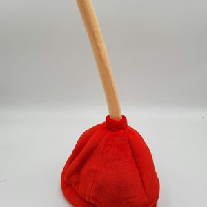 May include: A red and beige plush plunger hat. The hat is shaped like a plunger with a long, thin handle.