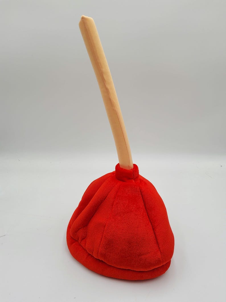 May include: A red and beige plush plunger hat. The hat is shaped like a plunger with a long, thin handle.