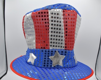 Puede incluir: Un sombrero rojo, blanco y azul con lentejuelas y un diseño de estrella. El sombrero tiene forma de sombrero de copa y tiene un ala ancha.