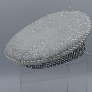 Pode incluir: Um chap&eacute;u branco brilhante com uma borda de p&eacute;rolas. O chap&eacute;u &eacute; decorado com strass.