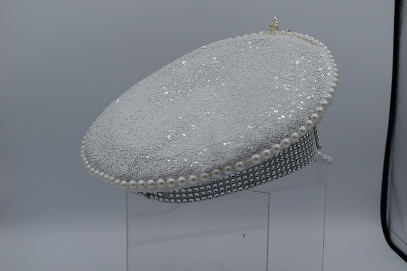 Pode incluir: Um chap&eacute;u branco brilhante com uma borda de p&eacute;rolas. O chap&eacute;u &eacute; decorado com strass.