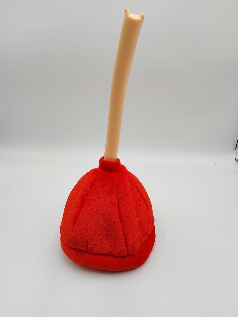 May include: A red plush plunger hat with a long, cream-colored handle. The hat is shaped like a traditional plunger with a rounded top and a flat base.