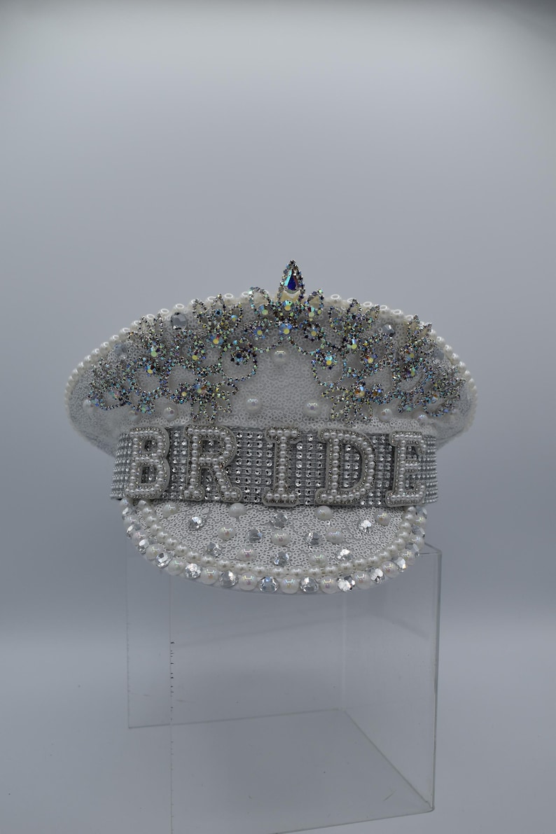Pode incluir: Chap&eacute;u de noiva branco decorado com p&eacute;rolas e strass. A palavra "BRIDE" &eacute; escrita em strass na frente do chap&eacute;u.