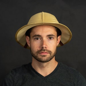 May include: A man wearing a khaki safari hat with a dark grey v-neck t-shirt.