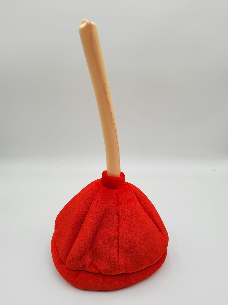 May include: A red and beige plush plunger hat. The hat is shaped like a plunger with a long, thin handle.