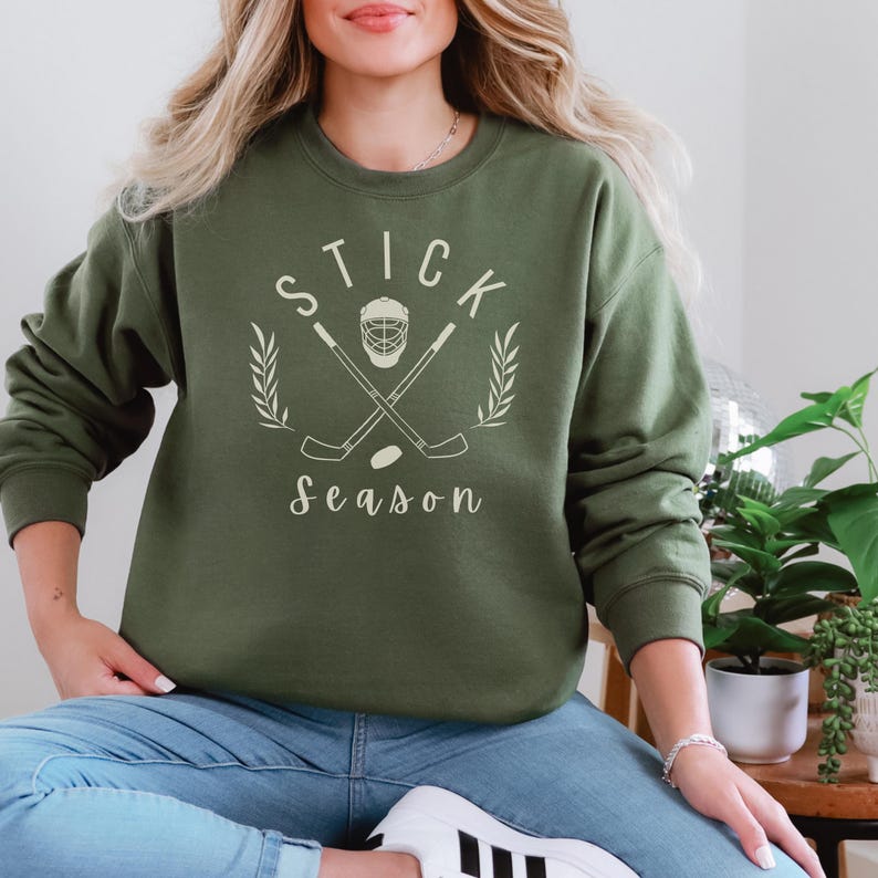 May include: A green sweatshirt with a white graphic design of hockey sticks crossed with a hockey helmet and the text "STICK Season".