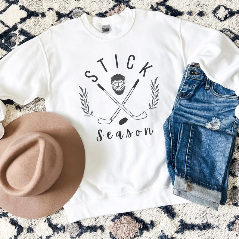 May include: White sweatshirt with a black graphic design of two hockey sticks crossed with a hockey mask and the text "STICK season".