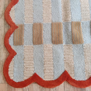 May include: A blue and beige checkered rug with an orange scalloped border. The rug is made of a soft, plush material.