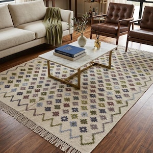 May include: A living room scene featuring a beige sofa, brown leather armchairs, and a marble coffee table with a gold base. A patterned rug with fringe and a colorful geometric design covers the floor. A bar cart and artwork complete the decor.