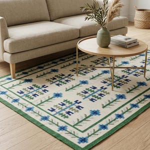 May include: A rectangular area rug with a cream background and a repeating floral pattern in blue and green. The rug has a green border and is placed on a hardwood floor. A beige sofa and a round wooden coffee table are in the background.