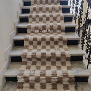 May include: A brown and white checkered rug is laid out on a set of stairs. The rug is made of a soft, fluffy material and has a subtle sheen. The stairs are made of marble and have a black trim. The text "Floor And Fabrics" is visible on the rug.