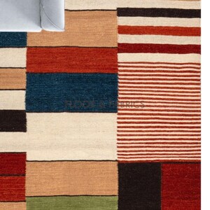 Op de afbeelding: Een rechthoekig vloerkleed met een geometrisch patroon. Het vloerkleed heeft kleurvlakken, waaronder rood, blauw, beige en bruin. Het vloerkleed heeft een textuur en is gemaakt van geweven stof. Geschikt voor een woon- of slaapkamer.