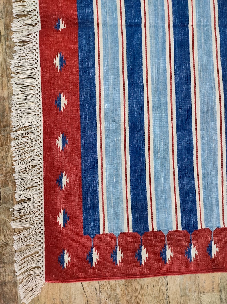 May include: A red, blue, and white striped rug with a fringe border. The rug has a geometric pattern in the border.