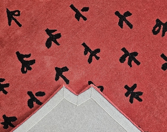May include: A red rug with a black pattern of stylized characters. The rug has a gray backing and is folded in half.