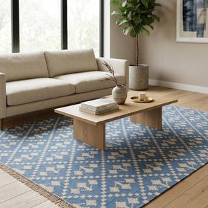 Puede incluir: Sal&oacute;n con un sof&aacute; beige, una mesa de centro de madera clara y una alfombra estampada azul y blanca. Tambi&eacute;n hay una maceta y obras de arte. La alfombra tiene un dise&ntilde;o geom&eacute;trico y un borde con flecos.