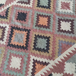 May include: A colorful rug with a geometric pattern in shades of brown, beige, pink, green, and black. The rug has a woven texture and a traditional design.