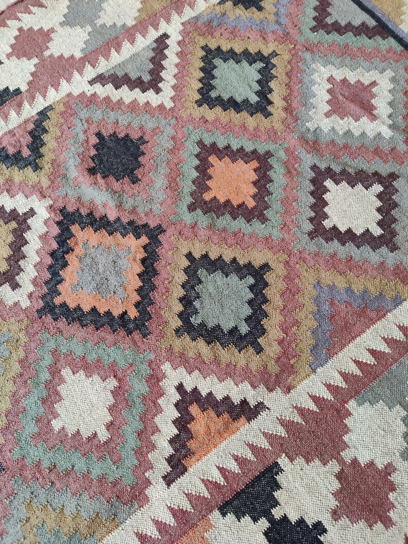 May include: A colorful rug with a geometric pattern in shades of brown, beige, pink, green, and black. The rug has a woven texture and a traditional design.