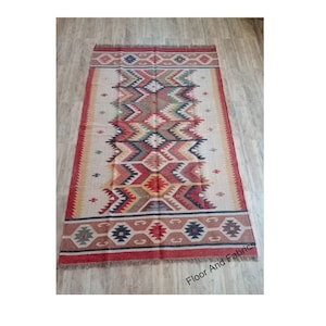 May include: A rectangular jute rug with a geometric pattern in shades of red, brown, beige, black, and green. The rug has a fringe border.