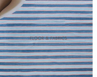 Peut inclure: Un tapis rayé bleu et rose avec des franges blanches. Le tapis a un léger brillant et est fait d'un matériau doux et tissé. Le texte "FLOOR & FABRICS" est visible au centre du tapis.