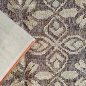 May include: A close-up of a brown and beige patterned fabric with a book corner in the lower left corner.
