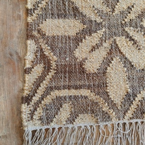 May include: A brown and beige woven rug with a geometric pattern and fringe on the bottom edge.
