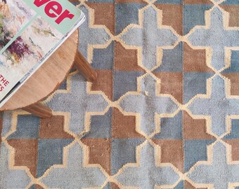Könnte beinhalten: Ein blauer und brauner geometrisch gemusterter Teppich mit einem Magazin auf einem Holzhocker.