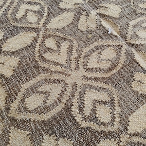 May include: Close-up of a woven rug with a brown and beige pattern. The rug has a textured surface and a repeating design of interlocking circles.